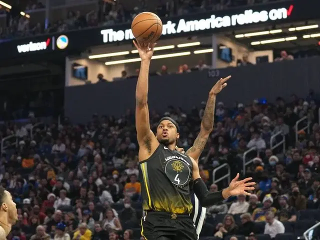 The image shows a man shooting a basketball in front of a crowd of people in a stadium. The man is...