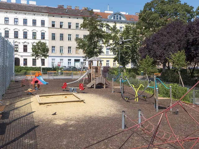 The image shows a playground in the middle of a city with a metal fence on the left side and a...
