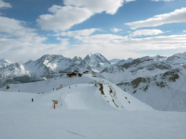 The image shows a group of people skiing down a snow covered slope with majestic mountains in the...