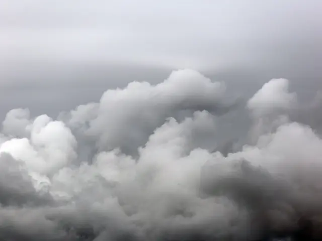 The image shows a view of the sky from the top of a hill, with white, fluffy clouds scattered...