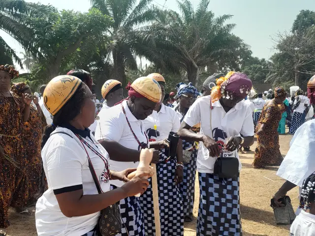 The image shows a group of women standing next to each other on a dirt field, wearing white and...