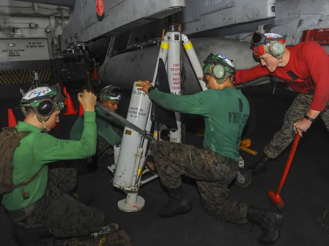 The image shows a group of men in green shirts and helmets working on a missile, surrounded by...