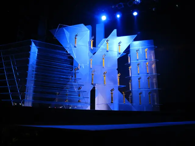 The image shows a stage set up for an awards ceremony, with a dark background and a few lights...