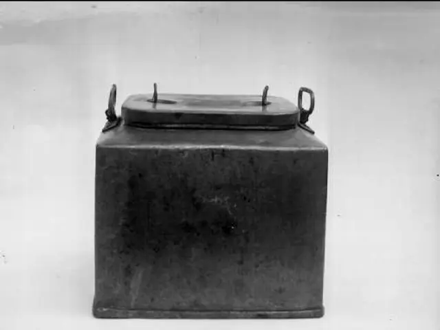 The image shows a black and white photo of a metal box with a lid, which appears to be a milk can....