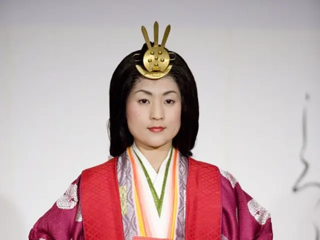 The image shows a woman in a traditional Japanese kimono standing on a runway. She is wearing a...