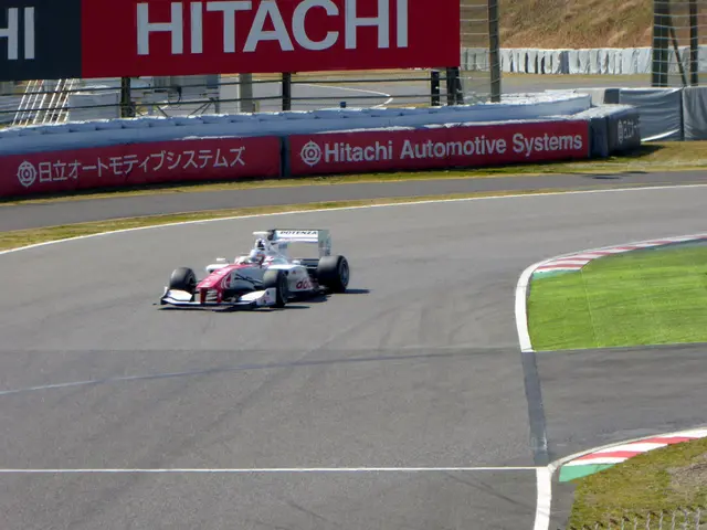 The image shows a Formula car driving down a race track with a sign that reads "Hitachi Automotive...