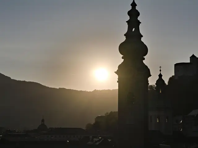 The image shows a clock tower in the middle of a city at sunset, surrounded by buildings and trees....