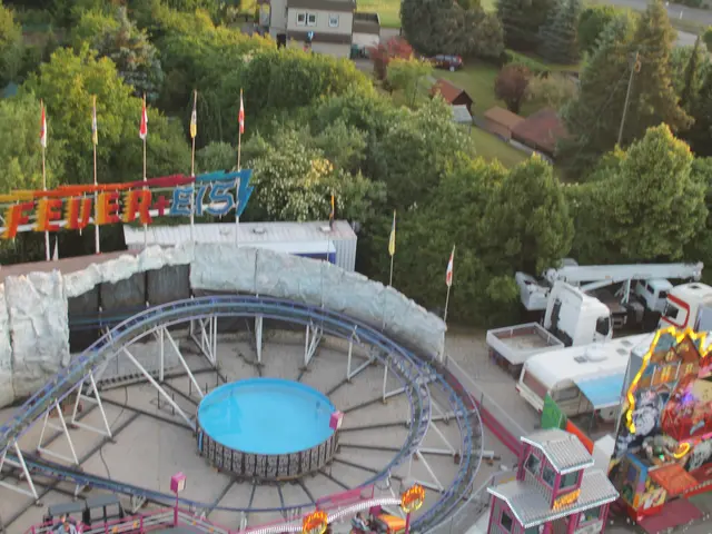 The image shows an aerial view of a ferris wheel in the middle of a park, surrounded by amusement...