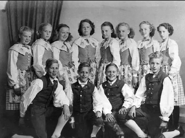The image shows a black and white photo of a group of children posing for a picture in front of a...