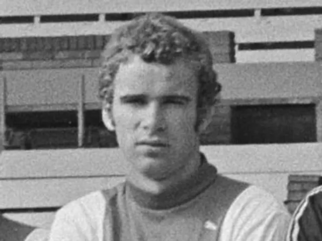 The image shows a black and white photo of a group of men standing next to each other, with a wall...