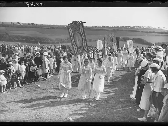 The image shows a group of people walking down a dirt road, some of them holding flags and...