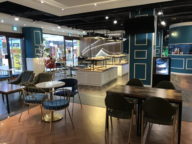 The image shows a restaurant with tables and chairs in front of a large window, illuminated by...