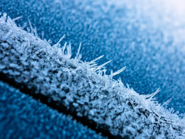 The image shows a close up of a car window covered in ice crystals, with a blue background. The ice...