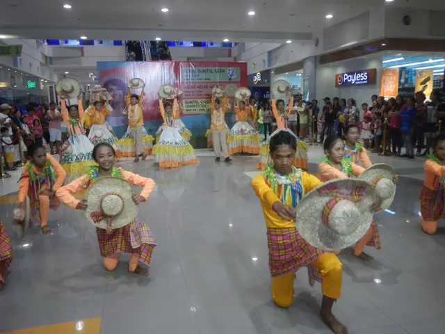 The image shows a group of young girls in colorful dresses and hats dancing in a mall, surrounded...