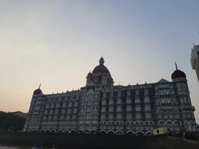 The image shows the Taj Mahal Palace Hotel in Mumbai, India. It is a large building with windows,...