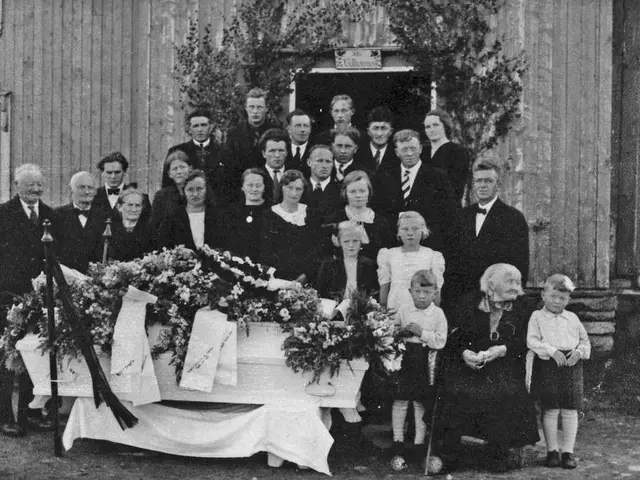 The image shows a group of people standing around a casket in front of a building, with a table...