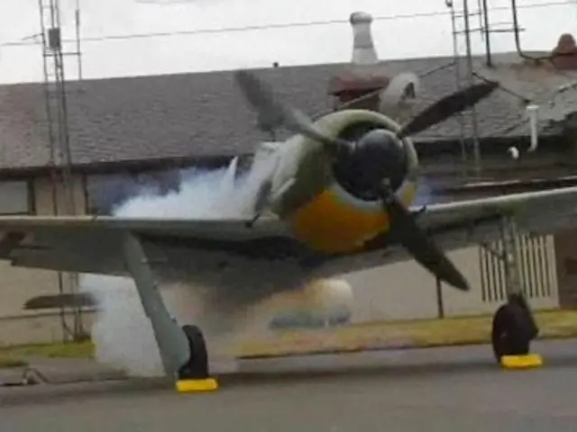 The image shows a small airplane taking off from an airport runway with smoke coming out of it. On...
