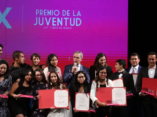 The image shows a group of people standing on top of a stage, smiling and holding certificates in...
