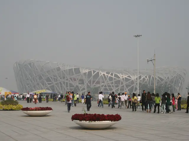 The image shows the Olympic Stadium in Beijing, China. There are many people walking around the...