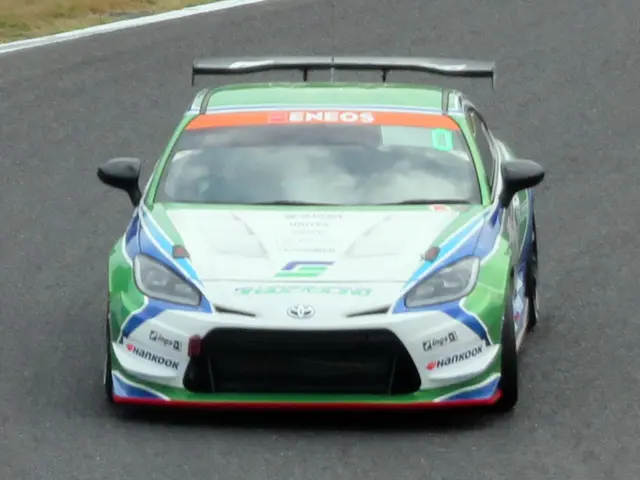 The image shows a Toyota GT86 race car driving on a race track, with text on the car and grass on...