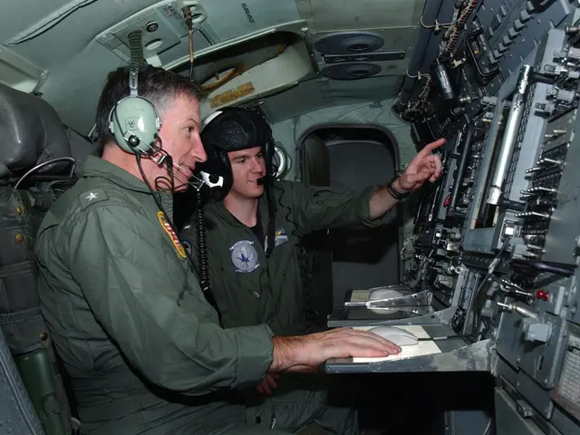 The image shows two men sitting in the cockpit of a plane, both wearing green uniforms and...
