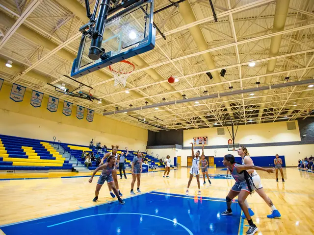 The image shows a group of women playing a game of basketball in a gymnasium. There are people...