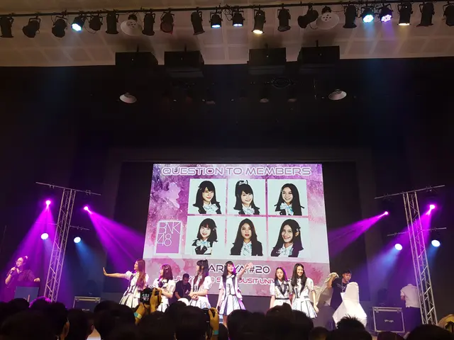 The image shows a group of people standing on top of a stage, illuminated by bright lights and...