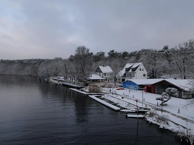 The image shows a picturesque winter scene of a small town next to a body of water, with...