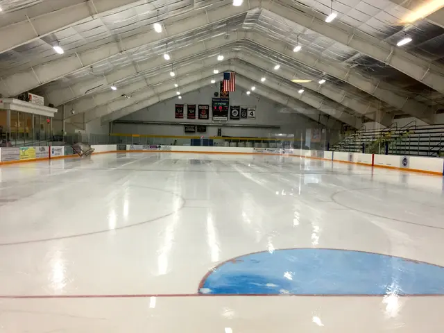The image shows a large indoor ice rink with a lot of lights on the ceiling, boards with text...