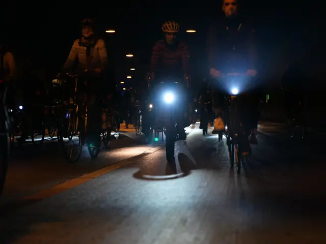 The image shows a group of people riding bicycles down a street at night, illuminated by the lights...
