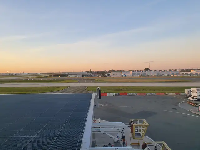 The image shows a view of an airport from the top of a building, with vehicles on the road below,...