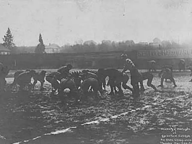 The image shows a black and white photo of a group of people playing football on a field, with...