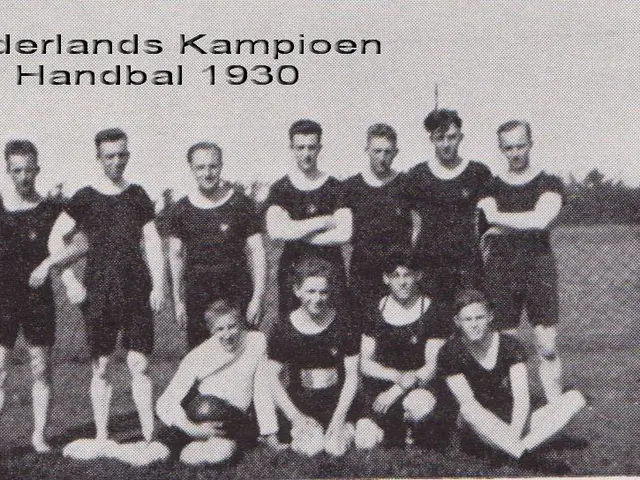 The image shows a black and white photo of a handball team from 1930, with a few people standing...