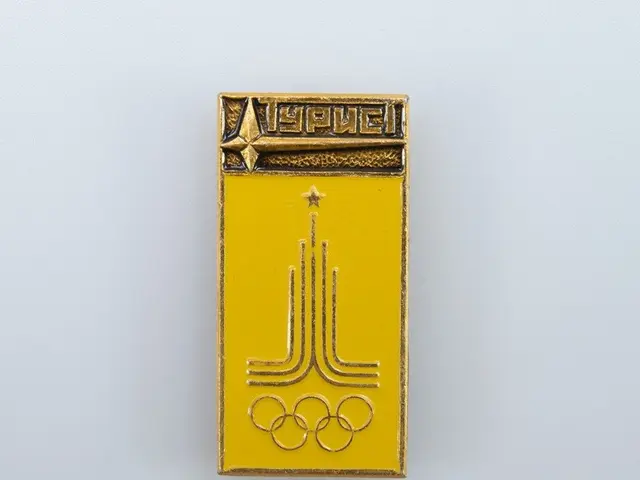 The image shows a yellow enamel pin with the Olympic logo on it, which is a badge of the USSR...
