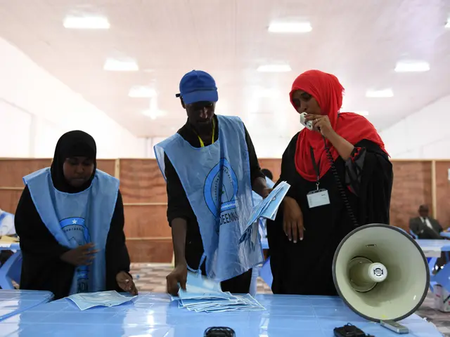 The image shows a group of people standing around a table with a megaphone, papers, and other...