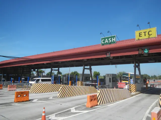 The image shows a toll booth with a sign that reads "Cash" on it, surrounded by vehicles on the...