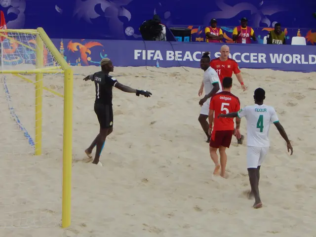 The image shows a group of men playing a game of beach volleyball on the sand. There is a net on...