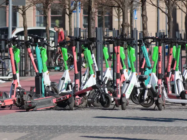 The image shows a row of electric scooters parked on the side of a street, with a person standing...
