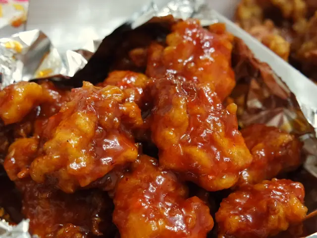 The image shows a close up of a bowl filled with buffalo wings covered in a red sauce. The wings...