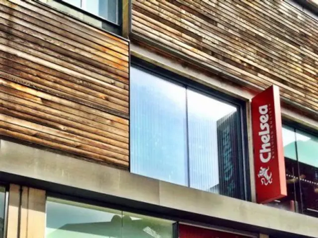 The image shows a building with glass walls and doors, banners with text and images, and a sign...