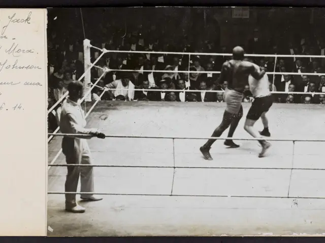 The image shows an old black and white photo of two boxers in a boxing ring, with a referee...