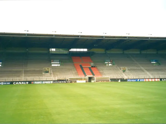The image shows a soccer field with lush green grass, a large stadium in the background, and a...