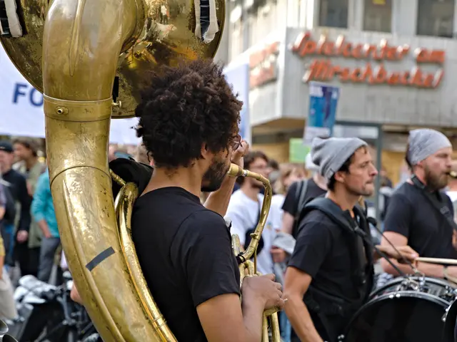 The image shows a group of people playing trombones in front of a crowd. There is a person holding...