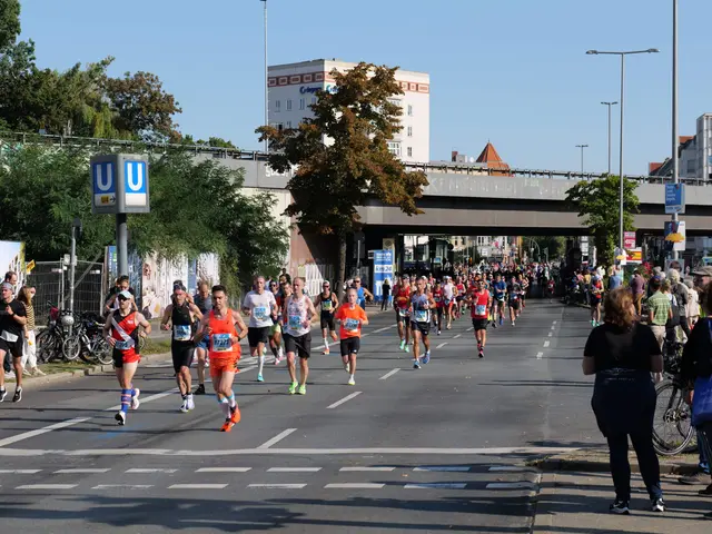 The image shows a group of people running in a marathon on a road surrounded by trees, light poles,...