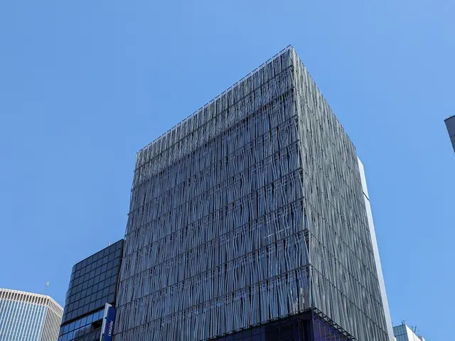 The image shows a bustling city street in Tokyo, Japan, with tall buildings in the background....