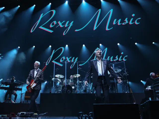 The image shows a group of people on stage playing musical instruments, with mics and stands set up...