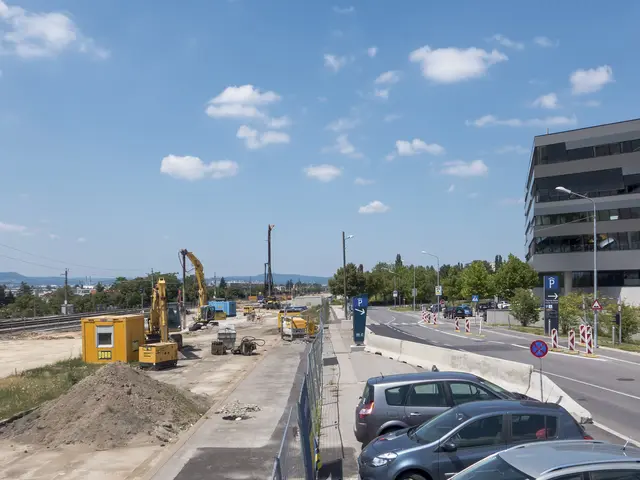 The image shows a construction site with cars parked on the side of the road, surrounded by...