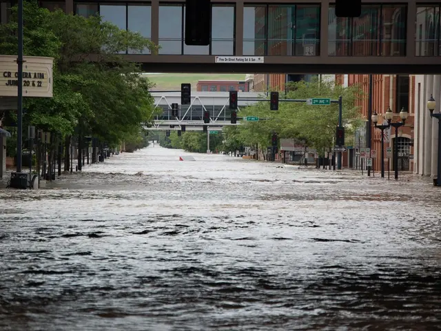 The image shows a flooded street in the middle of a city, with water covering the road, poles,...
