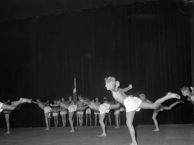 The image shows a group of people doing gymnastics on a stage in front of a curtain and a flag. The...