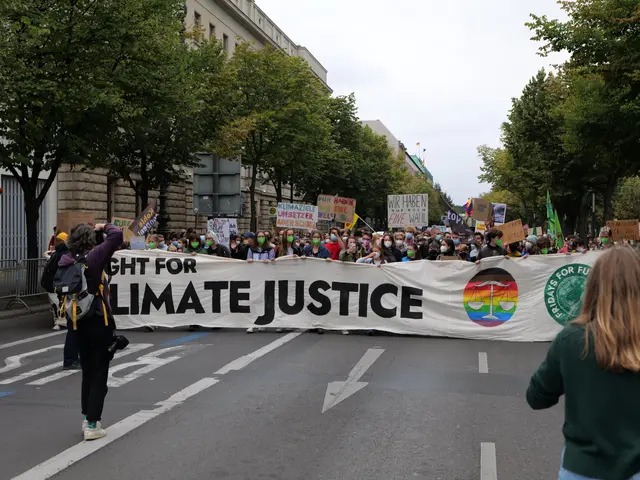 The image shows a group of people walking down a street, holding a banner with text on it. There...
